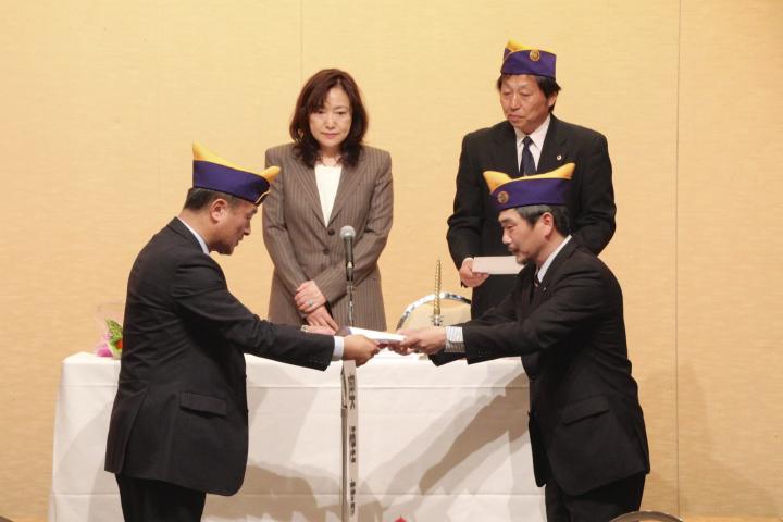 幹事L片岡博(右下)からスポンサー証明書を受け取るL澤谷幸弘(左下)。